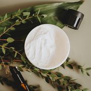 Crema cosmética en tarro abierto rodeada de hojas de eucalipto